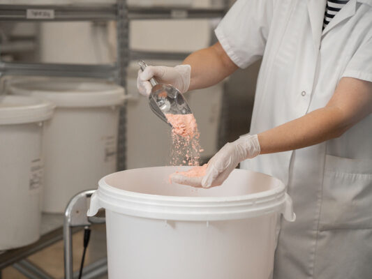Rohstoffherstellung in der SEEWALD Produktion – Dosierung von rosa Pulver in Mischbehälter mit Handschuhen
