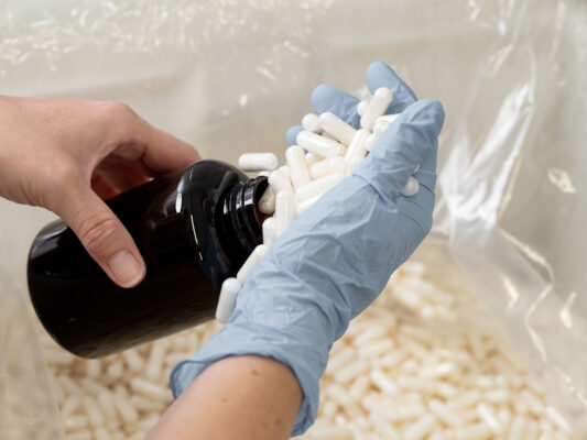 Handabfüllung von weißen Kapseln in Braunglasflasche mit Schutzhandschuhen in der SEEWALD Produktion